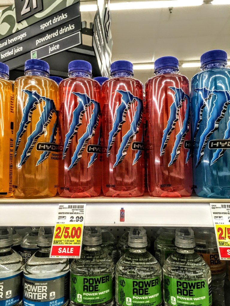 A store shelf displaying bottles of Monster Manic Mellon drinks. 